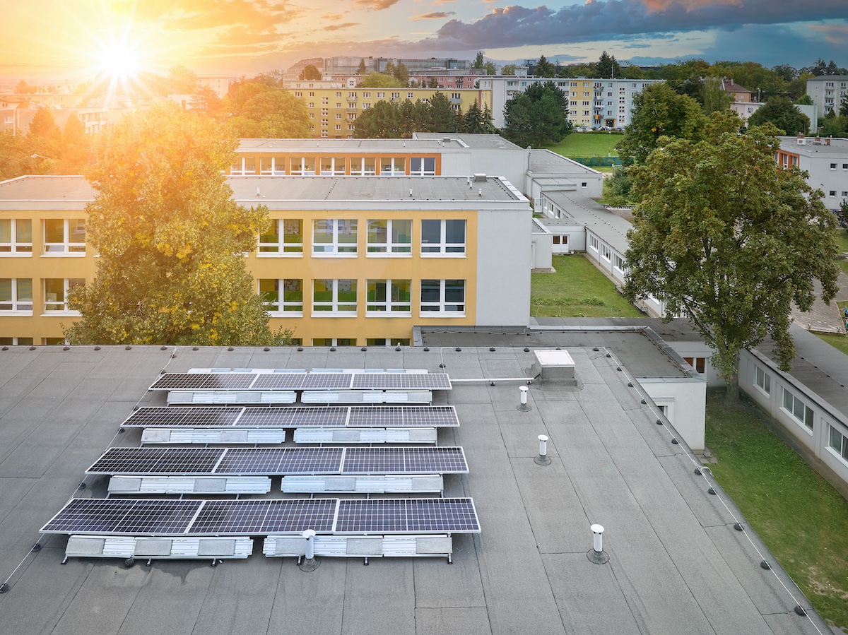 Solar power plant on the school roof. View of the photovoltaic panels against the school buildings, orange and blue colors. Fighting the energy crisis.